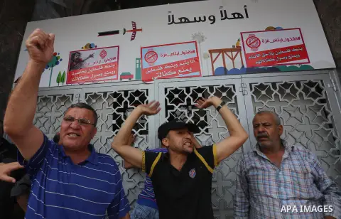 Palestinian relative of orphans and disabled hold banners during a protest against Palestine Bank policy on the closure of the accounts of charities in Gaza city on May 19, 2015. Photo by Mohammed Asad