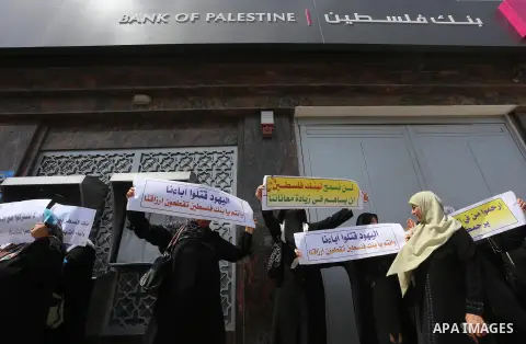 Palestinian relative of orphans and disabled hold banners during a protest against Palestine Bank policy on the closure of the accounts of charities in Gaza city on May 19, 2015. Photo by Mohammed Asad