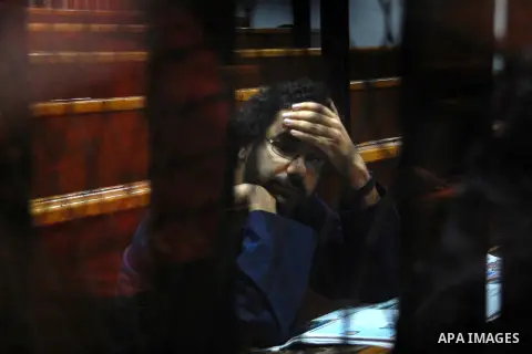 Egyptian activist and blogger Alaa Abdel Fattah looks on from behind the defendant's cage during his trial for insulting the judiciary alongside 25 other defendants including ousted Egyptian president Mohamed Morsi, who...