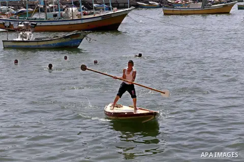 Palestinian youths swim into the Mediterranean Sea as they enjoy a warm day at the seaport in Gaza City on May 25, 2015. Photo by Mohammed Asad