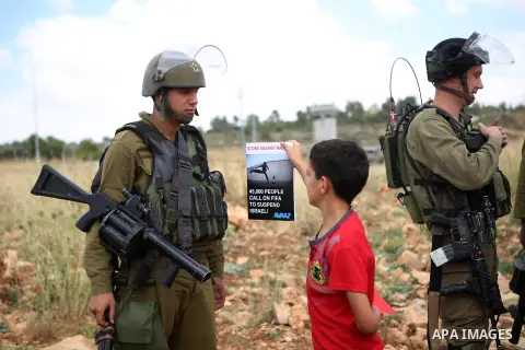 A Palestinian boy holds a banner in front of Israeli security forces during a demonstration against the Israeli Football Federation, in the West Bank village of Nabi Saleh, near Ramallah, 29 May 2015. The Palestinian Foo...
