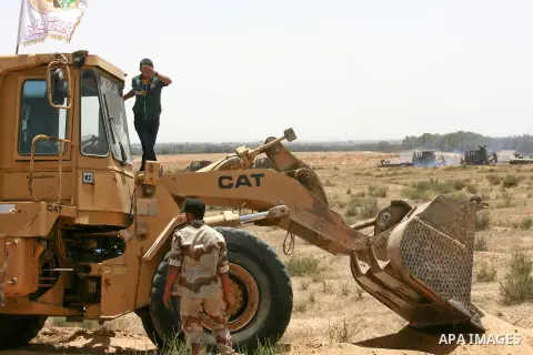 Palestinian militants of the Ezzedine al-Qassam Brigades, Hamas' armed wing, stand near a Palestinian bulldozer as they watch an Israeli bulldozers working along a barbed wire fence that separates Rafah in the southern G...