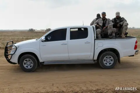 Palestinian militants of the Ezzedine al-Qassam Brigades, Hamas' armed wing, sit in the back of a pick-up truck watching Israeli bulldozers working along a barbed wire fence that separates Khan Yunis in the southern Gaza...