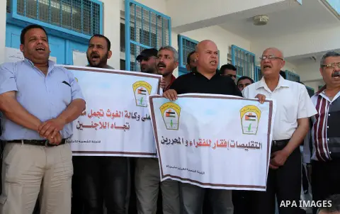 Palestinians hold banners during a protest against the UNRWA decision to reduce of the food aid in front of the headquarters United Nations Relief and Works Agency (UNRWA), in Rafah in the southern Gaza strip, June 11, 2...