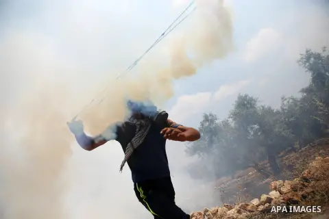 A masked Palestinian protester uses a slingshot to hurl back a tear gas canister fired by Israeli security forces during clashes following a demonstration against Jewish settlements in the West Bank village of Bilin, wes...