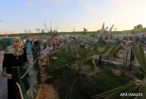 Palestinians stand watch a dinosaur model at the Sharm park in central Gaza Strip on June 17, 2015. Photo by Mohammed Asad