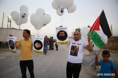 Palestinian protesters hold balloons and posters of prisoners during a protest demanding for their release from Israeli jails, outside Ofer Israeli military prison, near the West Bank city of Ramallah on June 27, 2015. P...