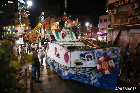 Palestinians walk next to a model of a ship during a rally in solidarity with activists aboard a flotilla of boats who are soon to set sail for Gaza in a fresh bid to break Israel's blockade of the territory, in the West...
