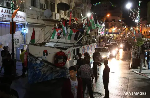 Palestinians walk next to a model of a ship during a rally in solidarity with activists aboard a flotilla of boats who are soon to set sail for Gaza in a fresh bid to break Israel's blockade of the territory, in the West...