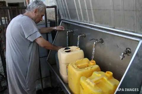 Palestinian children fill plastic bottles and jerry cans with drinking water from a public tap at the United Nations Relief and Works Agency (UNRWA) headquarters in the southern Gaza Strip refugee camp of Rafah on July 1...