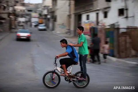 Palestinian children ride a bicycle in a street during power outage in Gaza city on July 27, 2015. Independent Commission for Human Rights warned Saturday of the aggravated humanitarian situation in Gaza due to continued...