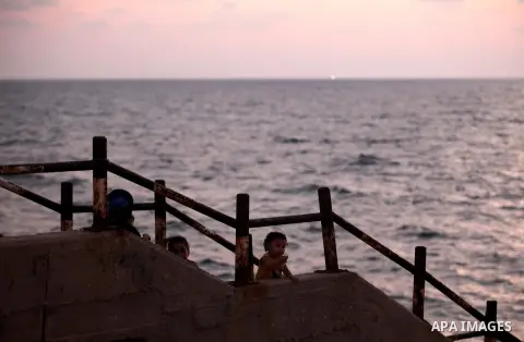 Palestinians sit outside their home, in front of the beach of Gaza city during the sunset, on July 27, 2015. Independent Commission for Human Rights warned Saturday of the aggravated humanitarian situation in Gaza due to...