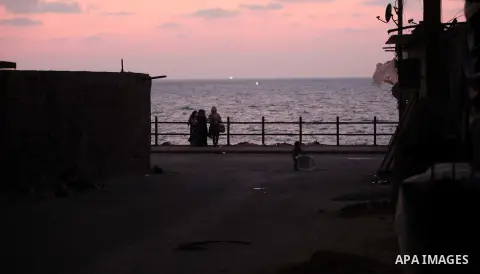 Palestinians sit outside their home, in front of the beach of Gaza city during the sunset, on July 27, 2015. Independent Commission for Human Rights warned Saturday of the aggravated humanitarian situation in Gaza due to...