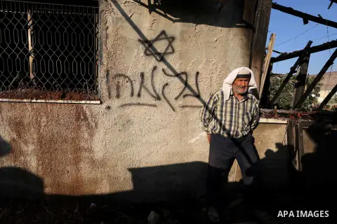 A Palestinian man walks past a graffiti reading in Hebrew 'revenge' on the wall of a house that was badly damaged from a suspected attack by Jewish extremists on two houses at Kafr Duma village near the West Bank city of...