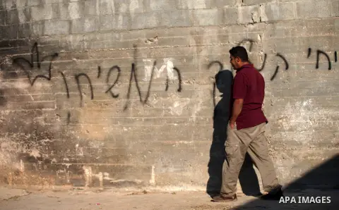A Palestinian man walks past a graffiti reading in Hebrew 'revenge' on the wall of a house that was badly damaged from a suspected attack by Jewish extremists on two houses at Kafr Duma village near the West Bank city of...