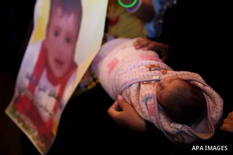 A Palestinian woman holds her child as she takes part in a protest demanding release the prisoners in Israeli jails, in front of Red cross office, in Gaza city, on on August 03, 2015. Photo by Ashraf Amra