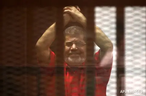 Ousted Egyptian president Mohammed Morsi waves as he stands behind bars during his trail in a court in Cairo on August 8, 2015. Cairo Criminal Court resumes on Saturday the trial of former Islamist president Mohamed Mors...