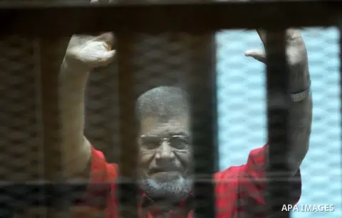 Ousted Egyptian president Mohammed Morsi waves as he stands behind bars during his trail in a court in Cairo on August 8, 2015. Cairo Criminal Court resumes on Saturday the trial of former Islamist president Mohamed Mors...