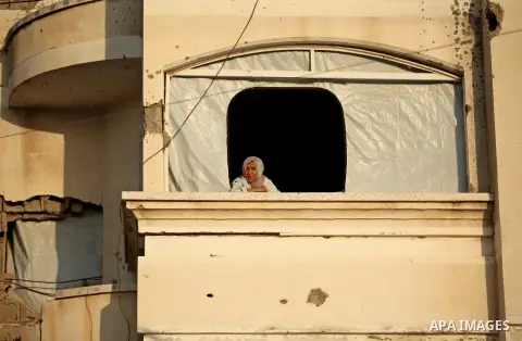 A Palestinian woman looks on from her destroyed house as members of Ezzedeen al-Qassam brigades, the armed wing of Hamas movement, take part in an anti-Israel parade in Beit Hanoun, in the northern Gaza Strip, on August...
