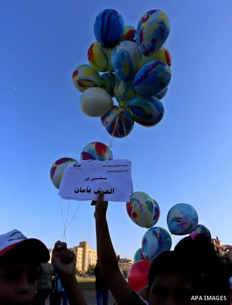 Palestinian children hold ballons during a protest against the Israeli blockade on the Gaza Strip and demanding for opening the Rafah crossing, outside the United Nations headquarter in Gaza city on August 12, 2015. Phot...