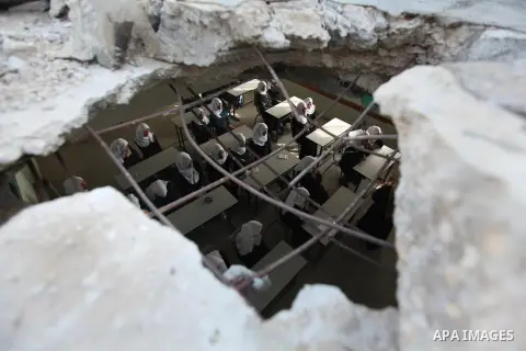 Palestinian schoolgirls, pictured through a hole in the roof of a classroom that witnesses said was damaged by Israeli shelling during a 50-day war last summer, attend a lesson on the first day of a new school year at Su...