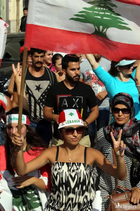 Lebanese protesters wave the national flag in front of a barbed wire fence during a demonstration, organized by "You Stink" campaign, to protest against the ongoing country's trash crisis in the capital Beirut on August...