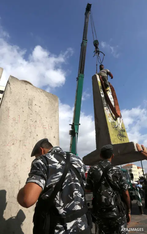 Municipality employees dismantle a concrete blast wall spread with graffiti depicting various political groups and bearing messages against police brutality in front of the seat of the government in central Beirut, on Au...