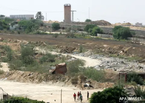 Palestinians walk in front the borders as bulldozers and diggers work on the Egyptian side of the border with the southern Gaza Strip town of Rafah, Sep. 1, 2015. Egypt has renewed its military campaign by digging up tun...