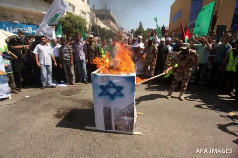 Palestinian Hamas militants burn a structure covered with a painting of an Israeli flag during a protest against the Israeli police raid on Jerusalem's al-Aqsa mosque on Tuesday, in Khan Younis in the southern Gaza Strip...