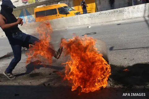 A Palestinian protester kicks a burning barrel during clashes with Israeli security forces following a demonstration against the Israeli police raid on Jerusalem's al-Aqsa mosque on Tuesday at the Israeli Qalandia checkp...