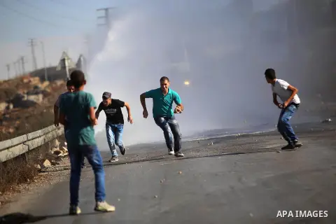 Palestinian protesters from the Jalazoun refugee camp run for cover from foul smelling water sprayed by an Israeli military vehicle during clashes following a demonstration against the Israeli police raid on Jerusalem's...
