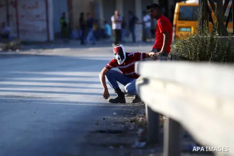 A Palestinian protester from the Jalazoun refugee camp takes cover during clashes with Israeli security forces following a demonstration against the Israeli police raid on Jerusalem's al-Aqsa mosque on Tuesday, on a road...