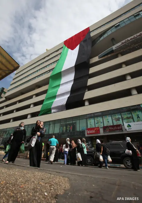 Palestinians walk past their national flag hanged on a building during an event to support Palestinian President Mahmoud Abbas in the West Bank city of Nablus on September 30, 2015. Abbas has circulated a hard-hitting cr...
