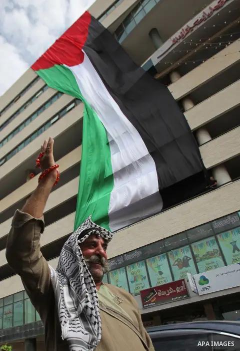 A Palestinian man flashes victory sign as he walks past his national flag hanged on a building during an event to support Palestinian President Mahmoud Abbas in the West Bank city of Nablus on September 30, 2015. Abbas h...