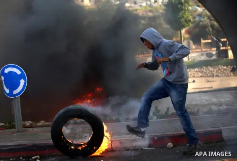 A Palestinian burns a tire during clashes with Israeli security forces in Beit El, near the West Bank city of Ramallah, on October 8, 2015. New violence rocked Israel and the Israeli occupied West Bank, including an inci...