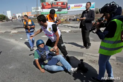 Medics help an injured Palestinian cameraman during clashes with Israeli security forces at the Hawara checkpoint, south of the West Bank city of Nablus, on October 11, 2015. An Israeli air strike in Gaza killed a pregna...