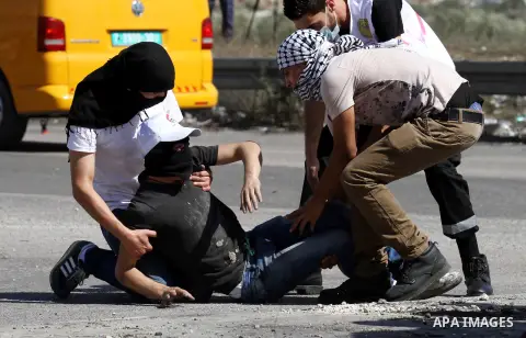 Masked Palestinian protestors help an injured comrade during clashes with Israeli security forces at the Hawara checkpoint, south of the West Bank city of Nablus, on October 11, 2015. An Israeli air strike in Gaza killed...