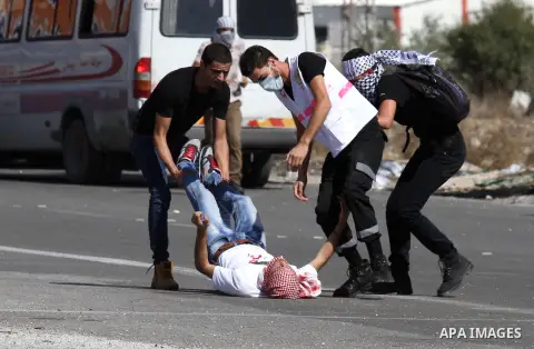Masked Palestinian protestors help an injured comrade during clashes with Israeli security forces at the Hawara checkpoint, south of the West Bank city of Nablus, on October 11, 2015. An Israeli air strike in Gaza killed...