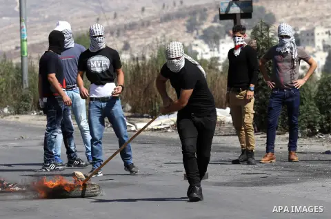 A masked Palestinian protester burns tires during clashes with Israeli security forces at the Hawara checkpoint, south of the West Bank city of Nablus, on October 11, 2015. An Israeli air strike in Gaza killed a pregnant...