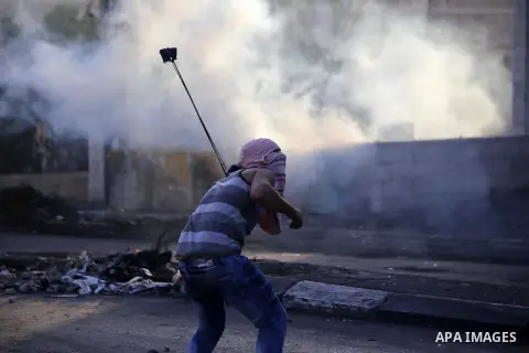 A Palestinian protester uses a sling shot to throw stones towards Israeli security forces during clashes in the West Bank town of Bethlehem, on October 11, 2015. Israeli security forces have arrested approximately 400 Pa...