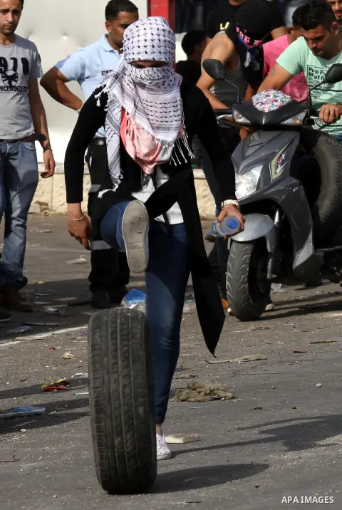 A female Palestinian protester kicks tires during clashes with Israeli security forces at the Hawara checkpoint, south of the West Bank city of Nablus, on October 12, 2015. Three new stabbings in Jerusalem and a car atta...