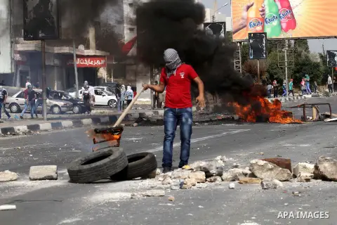 A masked Palestinian protester burns tires during clashes with Israeli security forces at the Hawara checkpoint, south of the West Bank city of Nablus, on October 12, 2015. Three new stabbings in Jerusalem and a car atta...