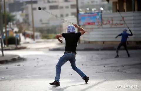 A Palestinian protester uses a slingshot to throw stones towards Israeli security forces during clashes in Beit El, on the outskirts of the West Bank city of Ramallah, on October 12, 2015. Three new stabbings in Jerusale...