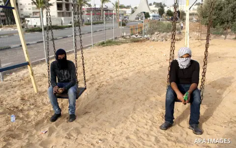 Palestinian protesters sit on a swing during clashes with Israeli security forces in Beit El on the outskirts of the West Bank city of Ramallah, on October 12, 2015. Three new stabbings in Jerusalem and a car attack spre...