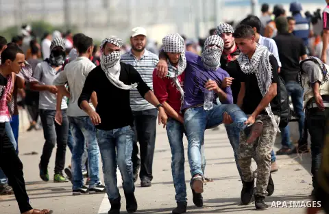 Palestinian protesters carry an injured comrade during clashes with Israeli security forces next to the border fence with Israel, at the Erez crossing in the northern Gaza strip, on October 13, 2015. A wave of stabbings...