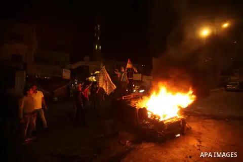 Palestinian youth stand next to a burning car belonging to an Israeli settler, that was set on fire by Palestinians as it entered the northern Palestinian West Bank city of Nablus, early on October 18, 2015, to visit and...