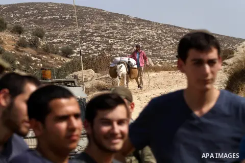 Israeli settlers stand in front of a farm as a Palestinian farmer works during the olive harvest season in the West Bank city of Nablus on Oct. 19, 2015. Photo by Nedal Eshtayah