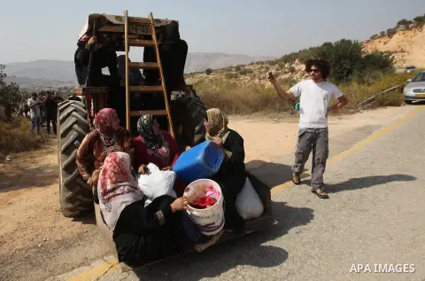 Palestinian farmers ride a tractor past Israeli settlers during the olive harvest season in the West Bank city of Nablus on Oct. 19, 2015. Photo by Nedal Eshtayah