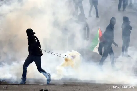 A Palestinian protester uses a sling shot to throw back a tear gas canister during clashes with Israeli security forces following a protest to mark the anniversary of the death of late Palestinian leader Yasser Arafat, i...