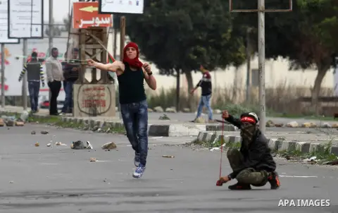 Palestinian protesters use a sling shot to throw stones towards Israeli security forces during clashes at the Hawara checkpoint, south of the West Bank city of Nablus, on November 28, 2015. The current wave of violence e...